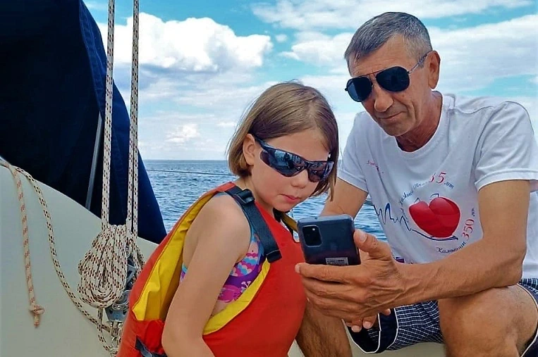Внучка и дедушка на яхте смотрят в экран телефона